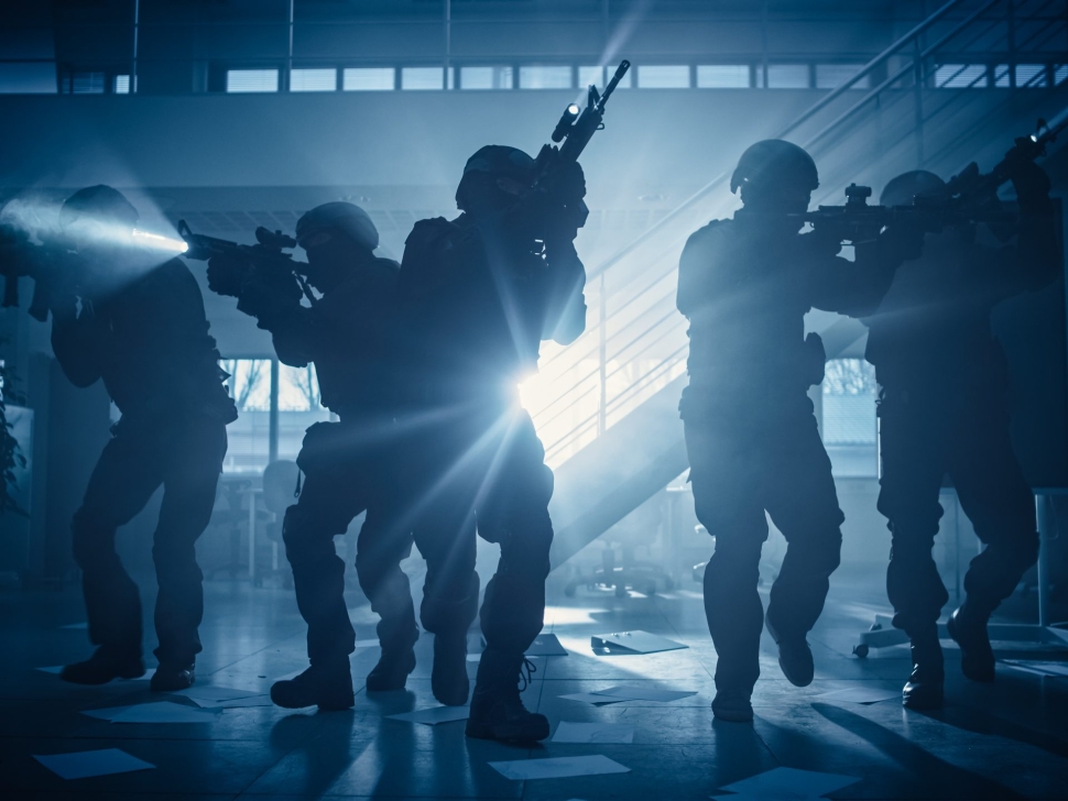 Masked Fireteam of Armed SWAT Police Officers Storm a Dark Seized Office Building with Desks and Computers. Soldiers with Rifles and Flashlights Move Forwards and Cover Surroundings.